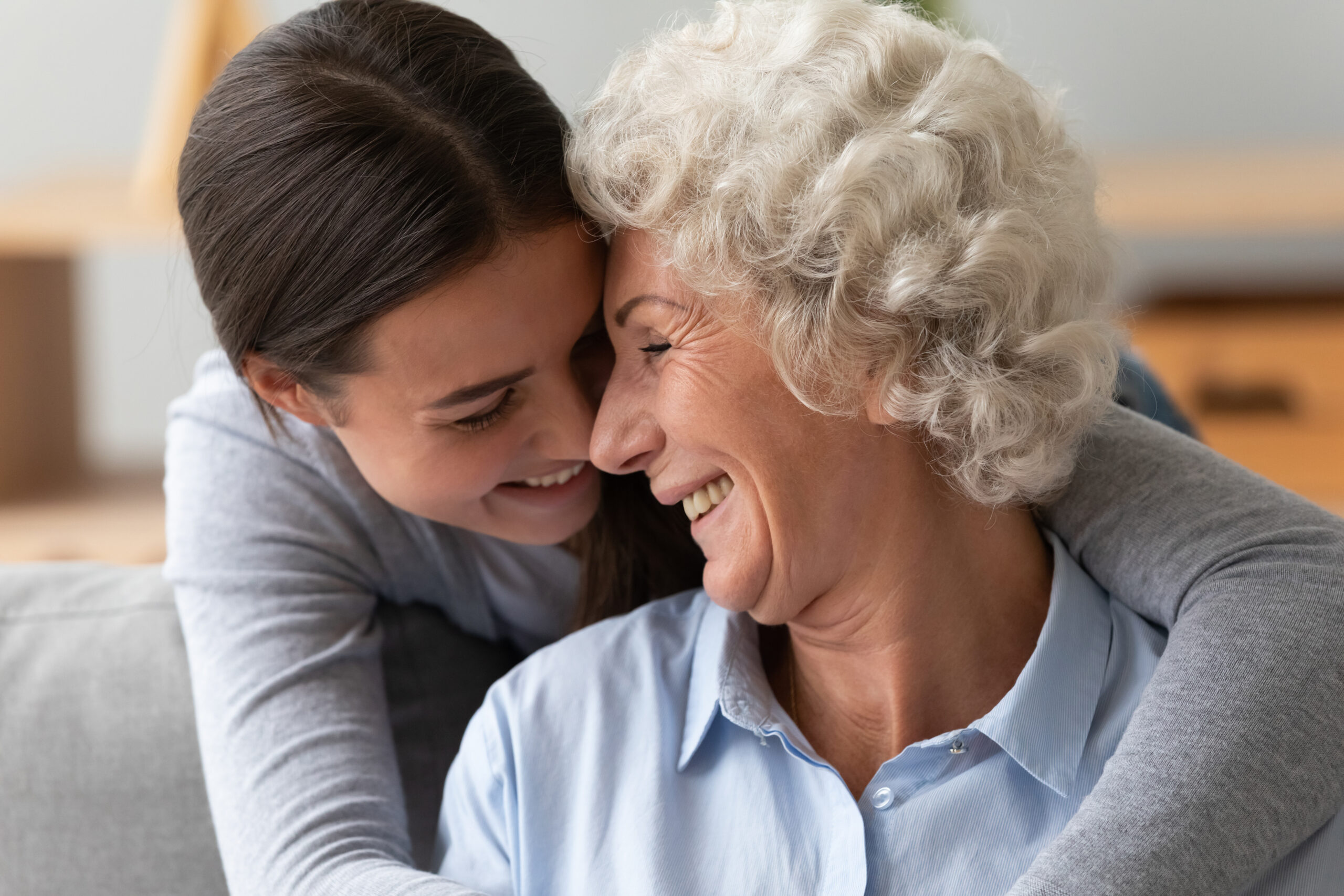 Close up happy grandmother and granddaughter touching noses, expressing love and support, enjoying tender moment together at home, looking at each other, young girl grandchild hugging granny